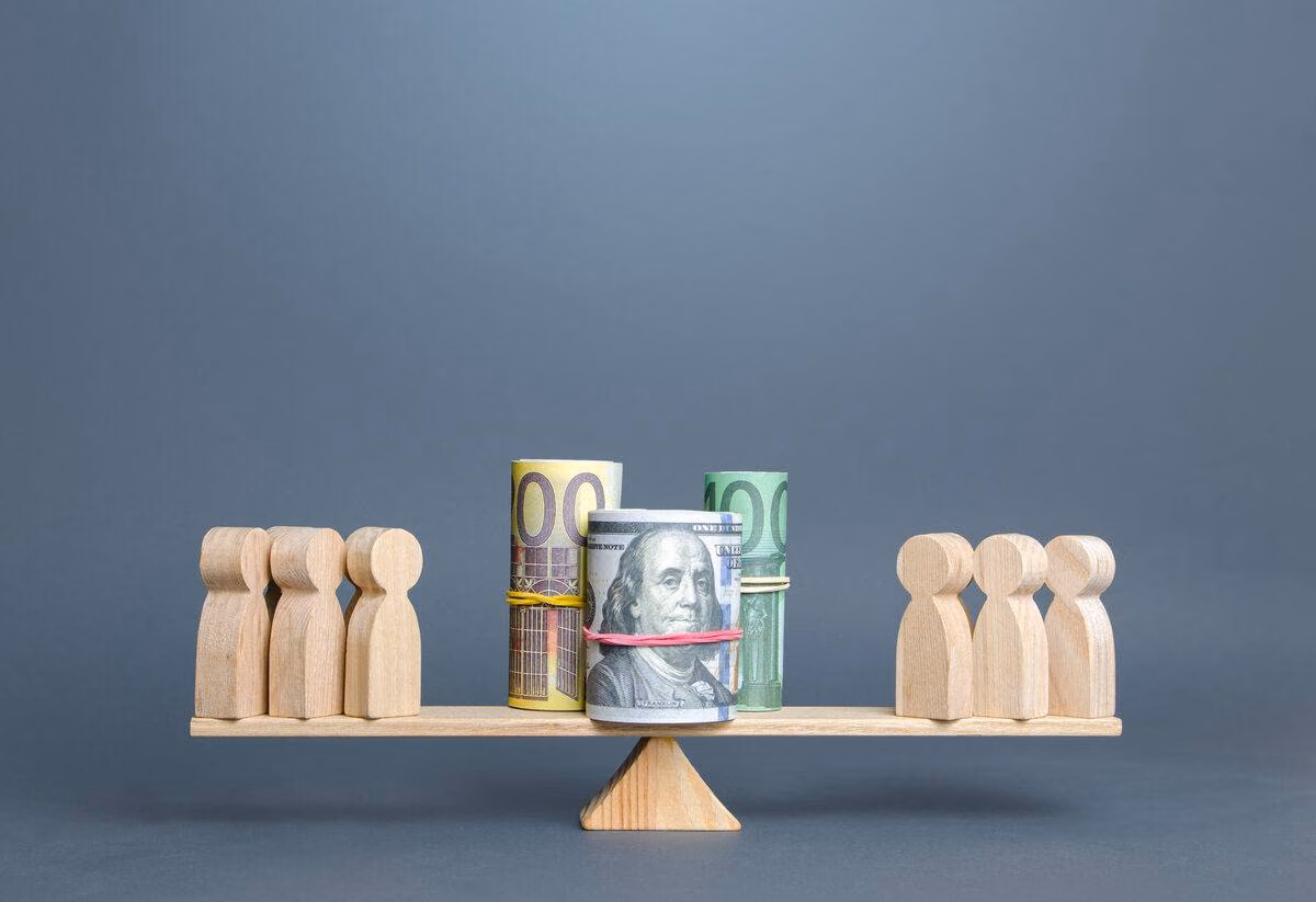 Wooden figures balance currency on a seesaw, symbolizing economic equality.