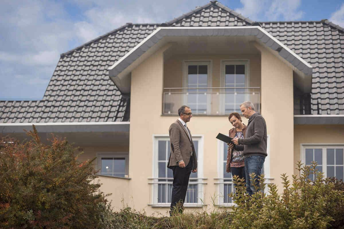 Three people in front of a modern house review documents, showing decision-making.