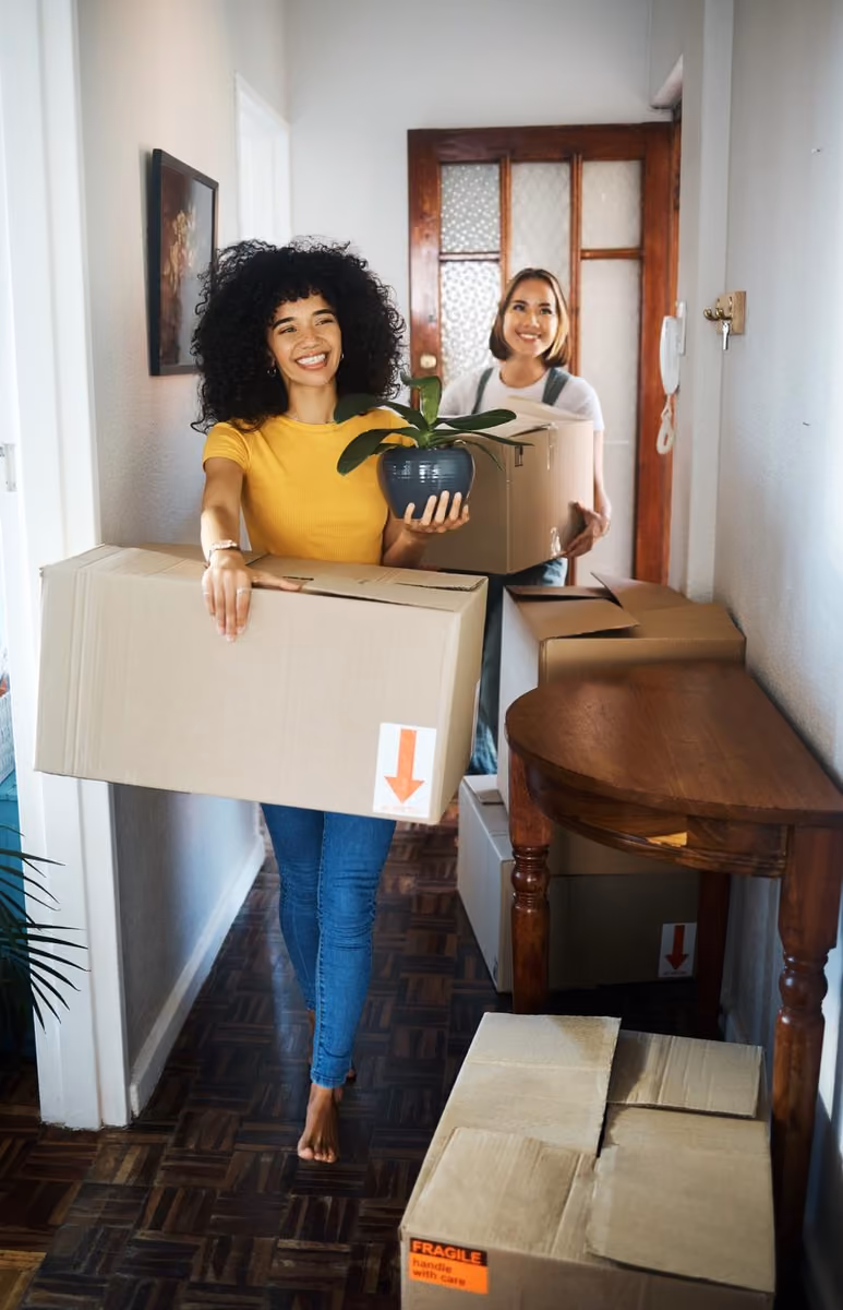 Two people carrying moving boxes into a new home